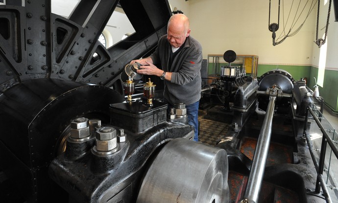 Ein Mann gießt Öl aus einer Kanne in einen von zwei Tropfölern der Dampfmaschine. Ein Mann gießt Öl aus einer Kanne in einen von zwei Tropfölern der Dampfmaschine.