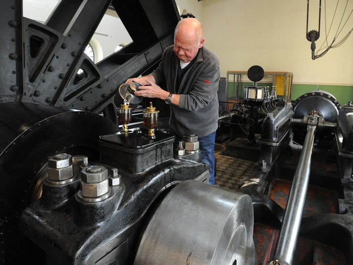 Ein Mann gießt Öl aus einer Kanne in einen von zwei Tropfölern der Dampfmaschine. Ein Mann gießt Öl aus einer Kanne in einen von zwei Tropfölern der Dampfmaschine.